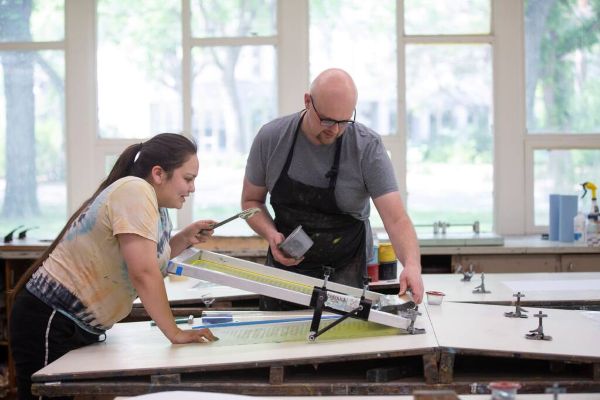 Instructor and student working with screen printing press in studio