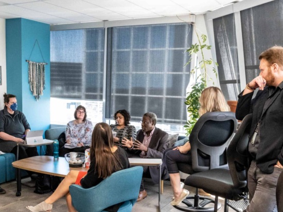 Small group discussion in a lounge‑style classroom, with people seated in chairs around a table.