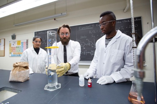Students in lab coats conducting a chemistry experiment in a classroom laboratory.