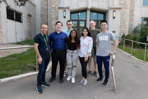 A group of people stand together outside a campus building for a casual group photo.