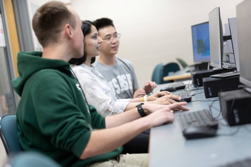 Students working together at desktop computers in a classroom or lab setting.