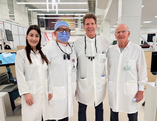 Four dental professionals in white lab coats standing together in a clinical laboratory.
