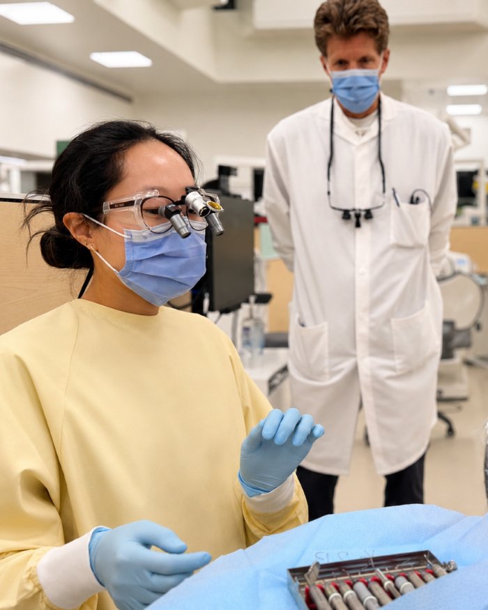 Dental student wearing magnification loupes prepares instruments in a clinical lab.