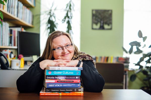 Person resting on stack of books titled on gender, queer cultures, and feminism in an office.