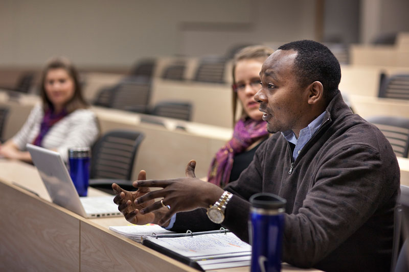 People discussing ideas with laptops and notebooks in a tiered lecture hall.