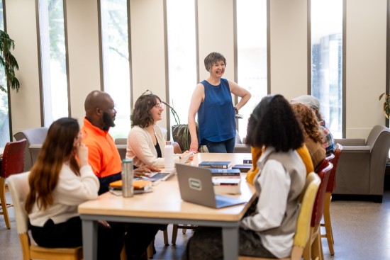 Students gather around a table for a collaborative discussion in a bright study space.