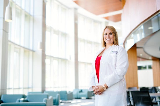 Woman with white lab coat standing in a bright College of Medicine atrium