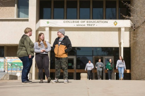 Students walk and talk on a sunny day in front of the College of Education building