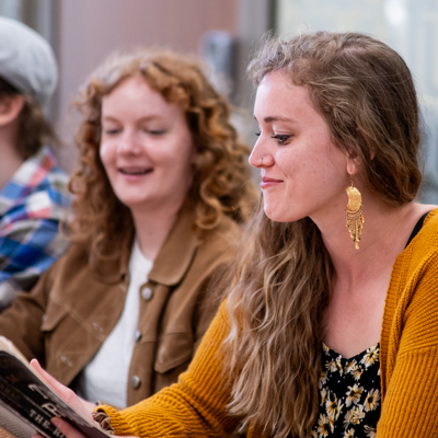 Students seated indoors reading books during a class or study session.